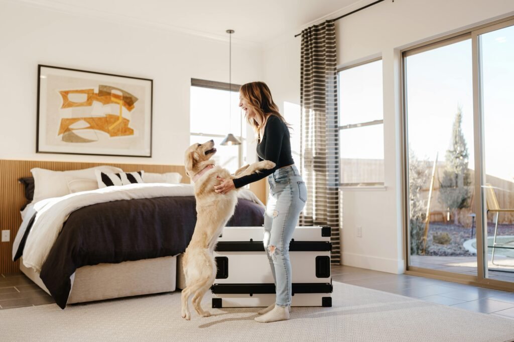 A woman joyfully interacts with her golden retriever in a sunlit bedroom, showcasing warmth and comfort.
